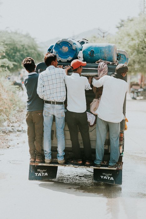 Travel photography of a group of men holding onto the back of a trailer in India.