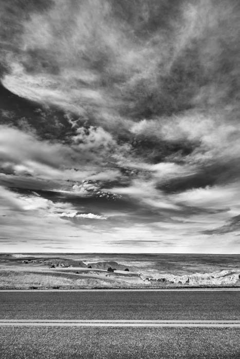 A black and white photography of a road and the clouds
