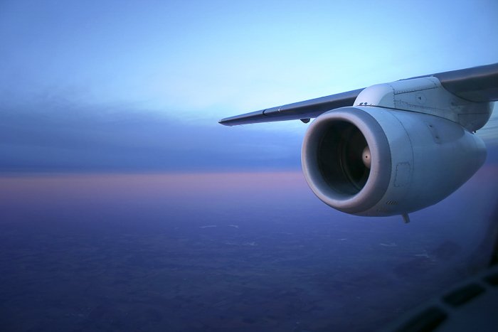 View from an airplane window of the airplane wing and engine, against a blue, purple, and orange dusk