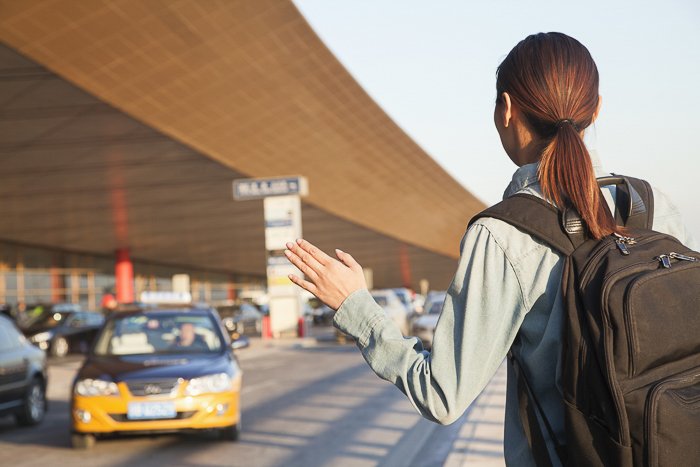 brunette woman with a backpack hailing down a taxi cab at the airport
